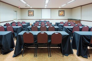 A conference room with rows of tables and chairs, a projector screen, and a carpeted floor. - Holiday Inn Express Hotel & Suites Dallas - Duncanville by IHG (Duncanville)