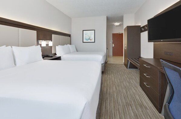 Quarto de hotel com duas camas, uma mesa, uma televisão e porta para o banheiro.