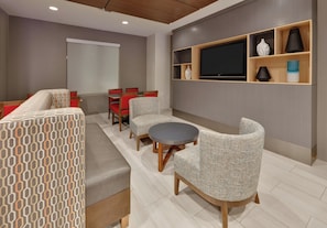 A modern living room with a sofa, chairs, a round table, and a TV mounted on the wall.