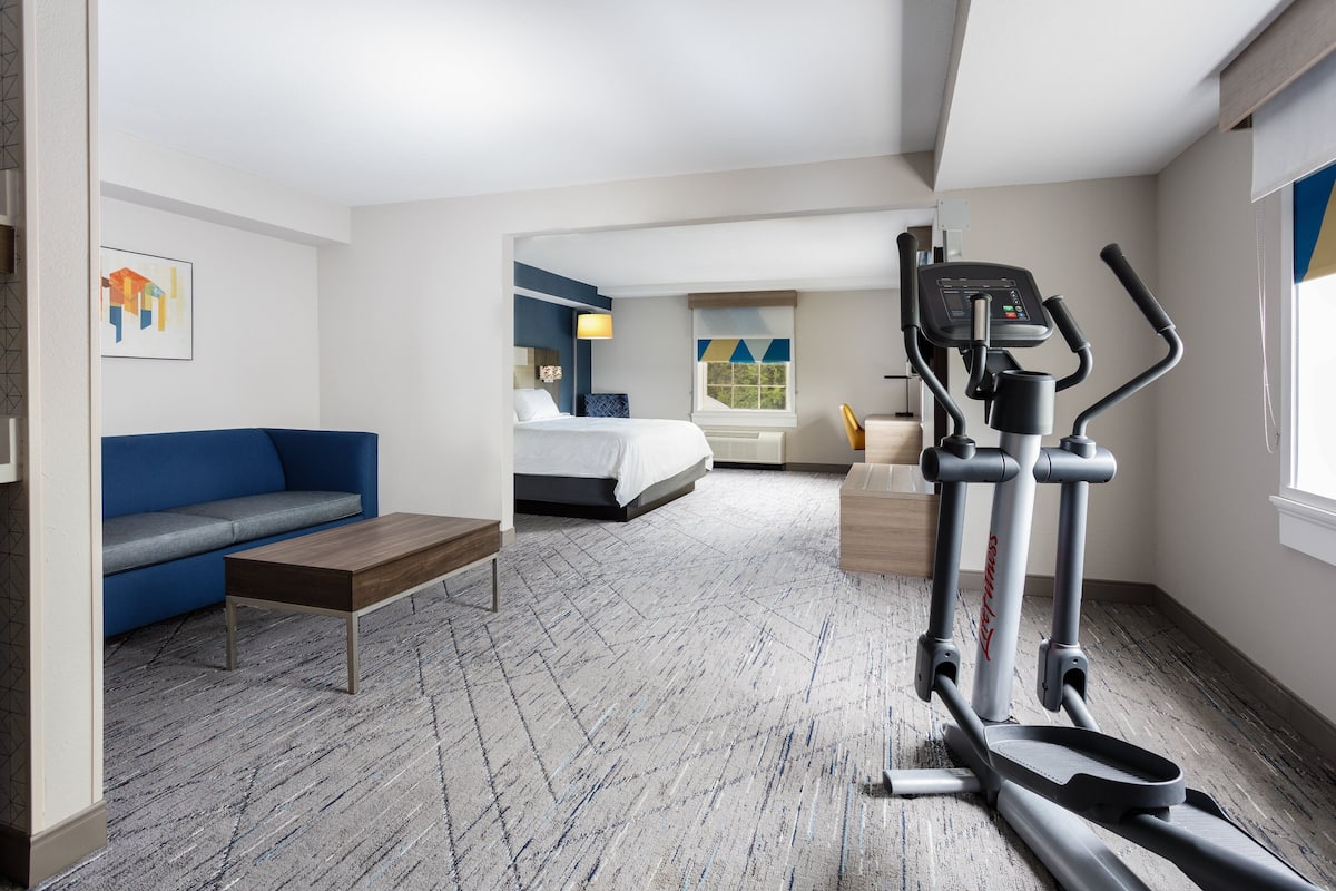 A hotel room with a bed, a blue sofa, a treadmill, and a desk.