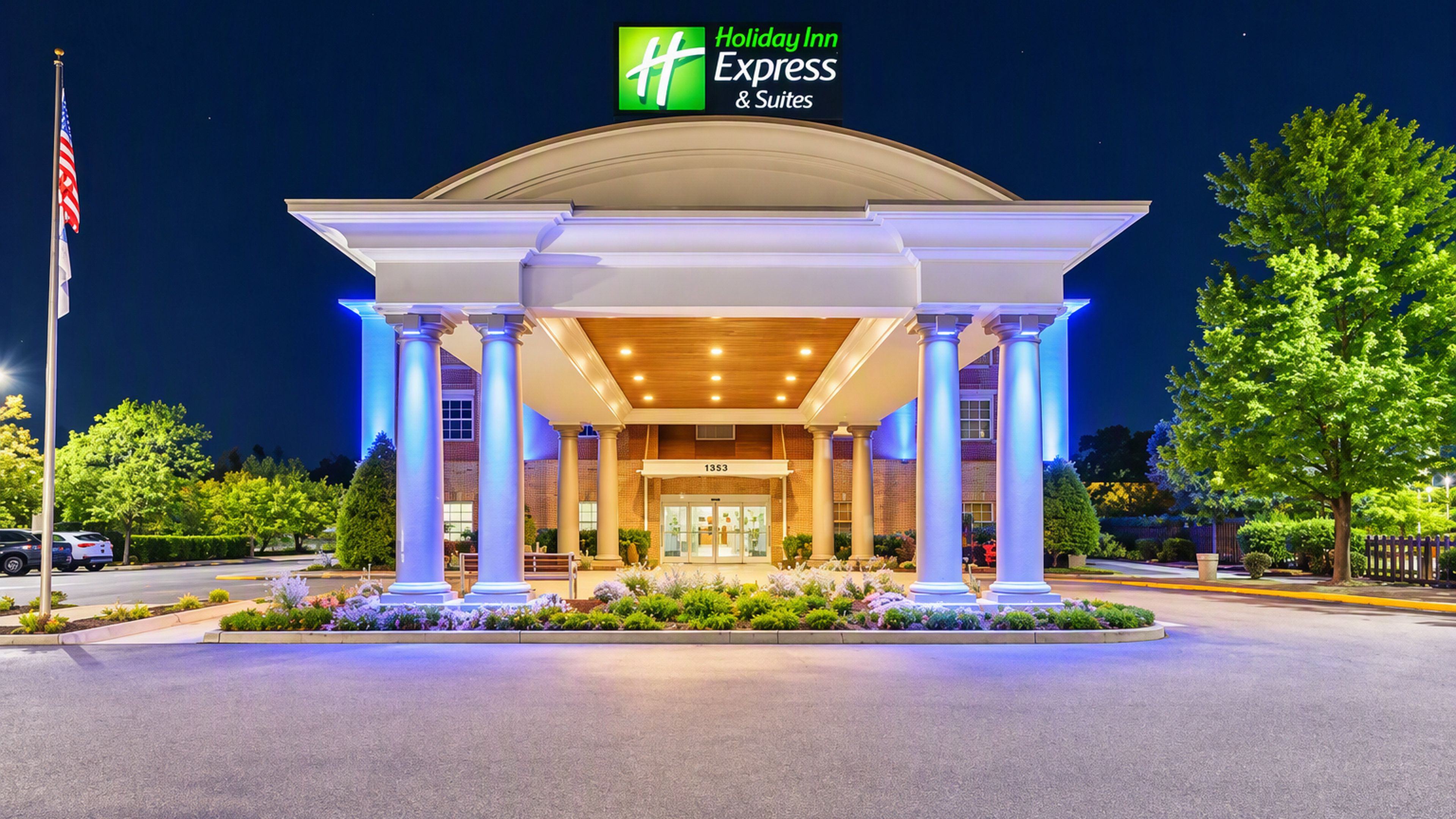 Un Holiday Inn Express & Suites con un diseño arquitectónico clásico, que presenta una entrada central con columnas, fachada de ladrillo y un área de entrada bien iluminada.