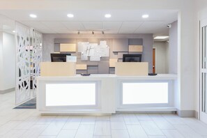 A modern reception area with a central desk, a decorative wall, and a security camera. - Holiday Inn Express & Suites Williamsburg by IHG (Williamsburg)