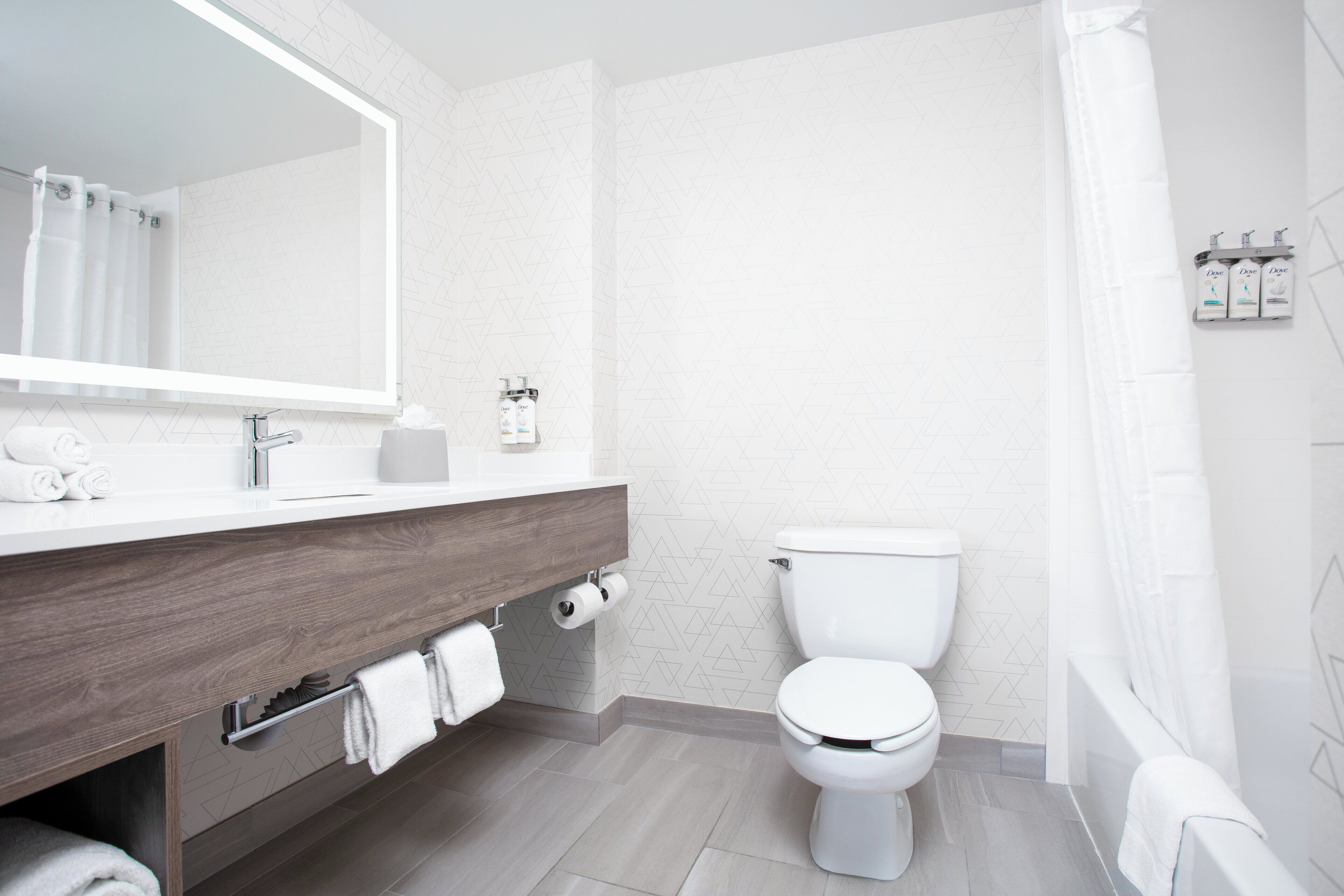 A modern bathroom with a wooden vanity, white toilet, and a shower area.