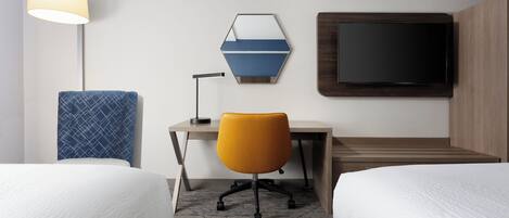 A hotel room with two beds, a desk, a chair, a TV, and a lamp.