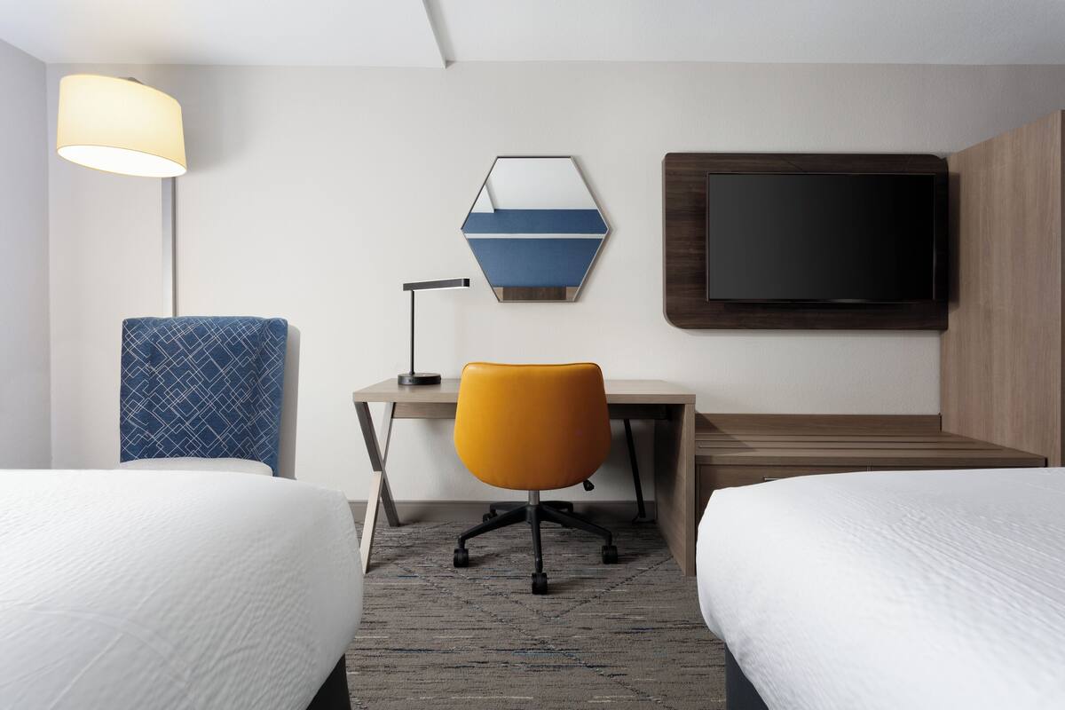 Una habitación de hotel con dos camas, un escritorio, una silla, un televisor y una lámpara.