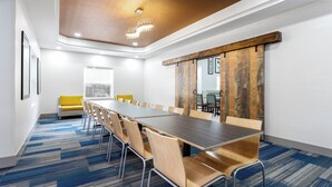 Una sala conferenze con un lungo tavolo, sedie, un divano e un grande pannello di legno alla parete.