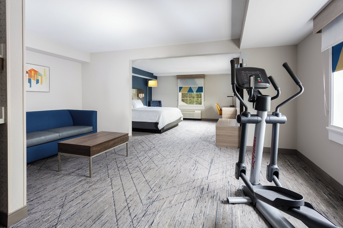 A hotel room with a bed, a blue sofa, a small table, a treadmill, and a window with a view.