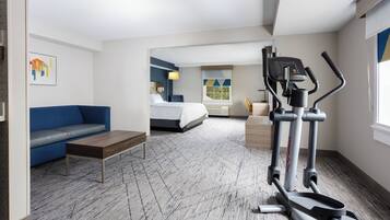 A hotel room with a bed, a blue sofa, a small table, a treadmill, and a window with a view.