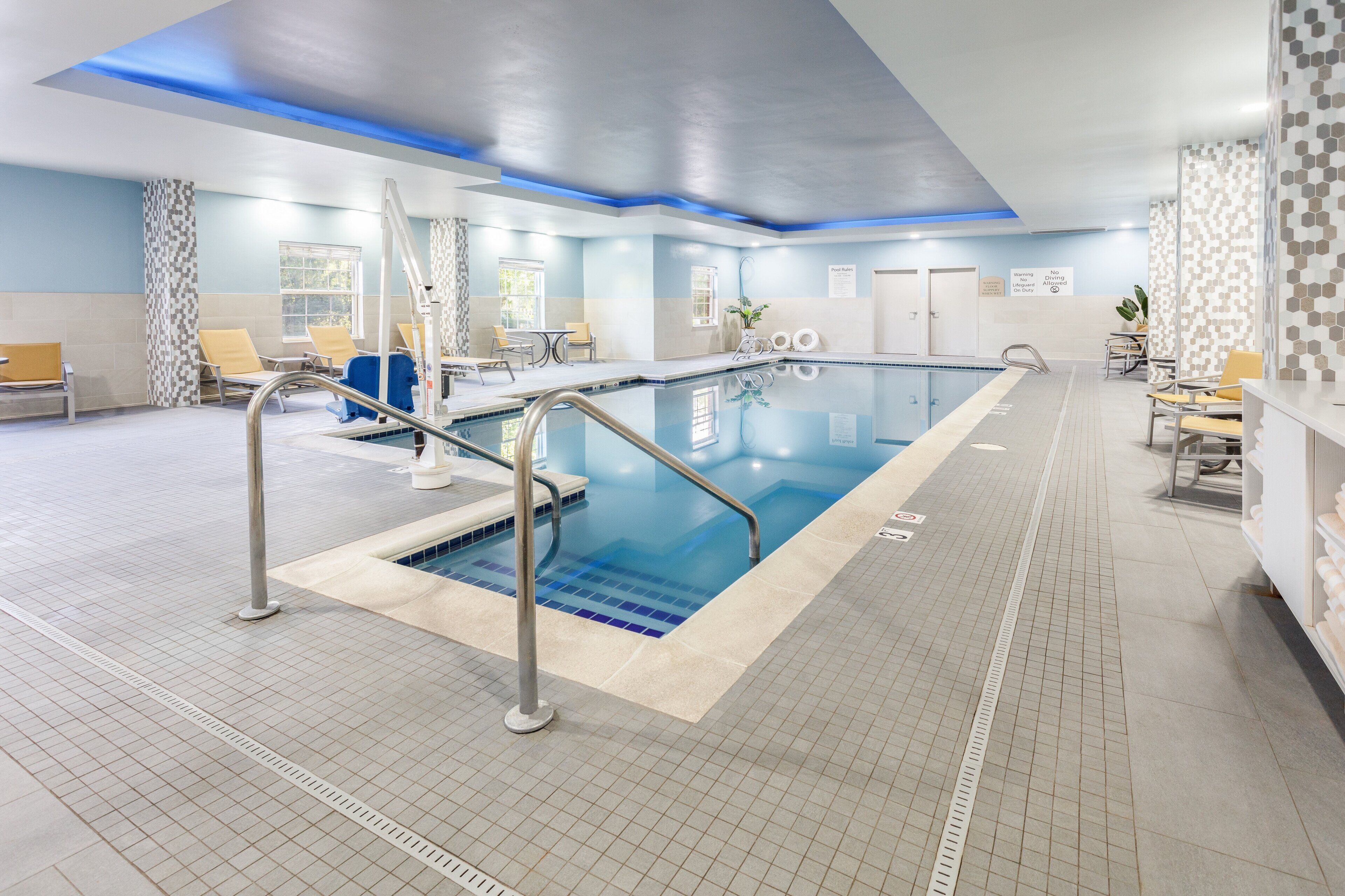 Una piscina interior con fuente de agua azul, una escalera de piscina y sillones de descanso.