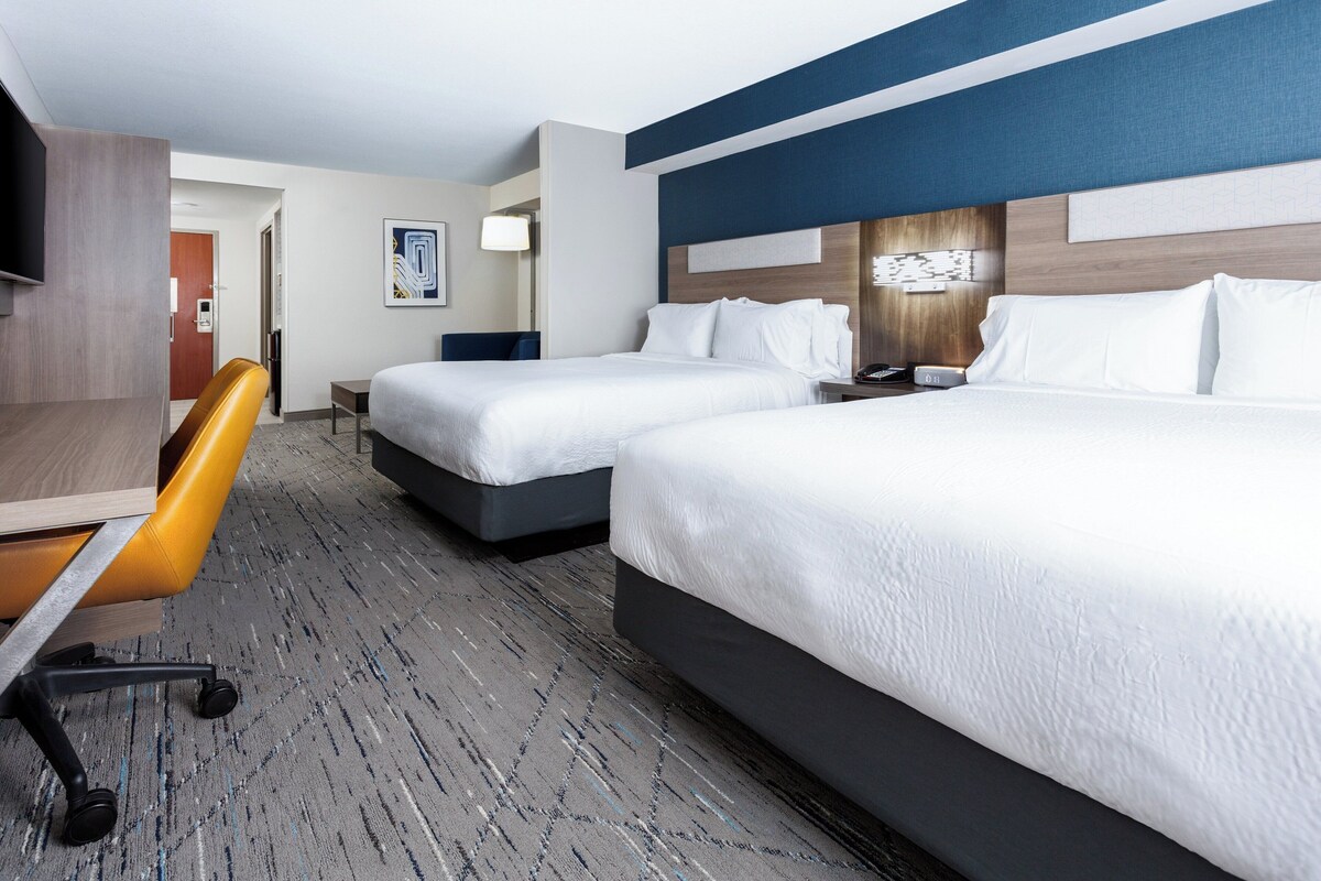 A hotel room with two beds, a desk, and a chair.