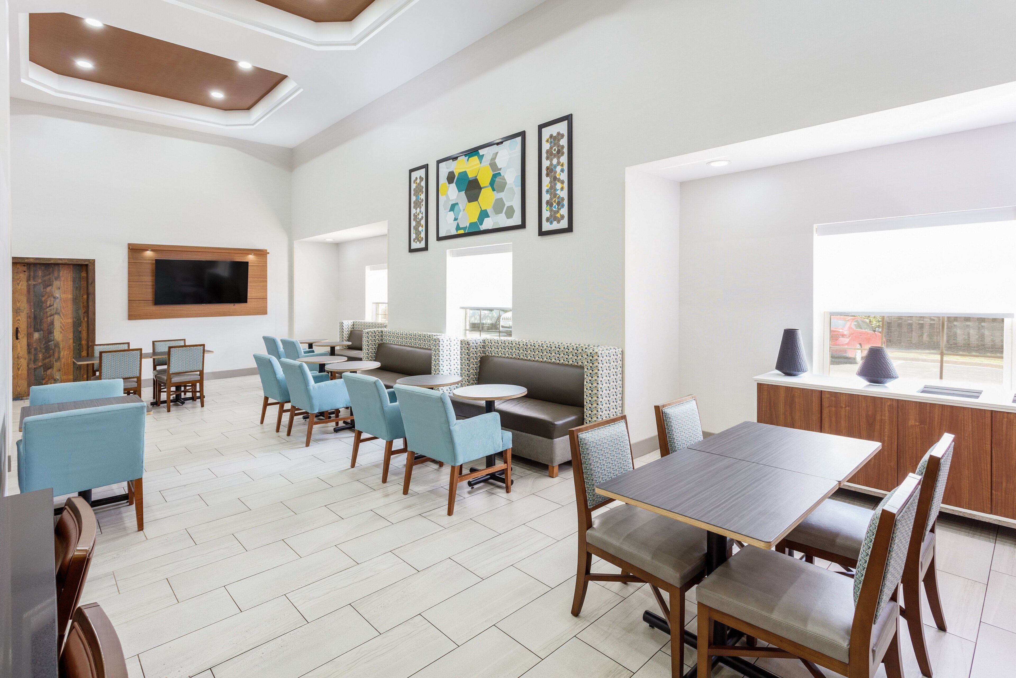A spacious dining area with multiple seating options, including tables and chairs, and a large window providing natural light.