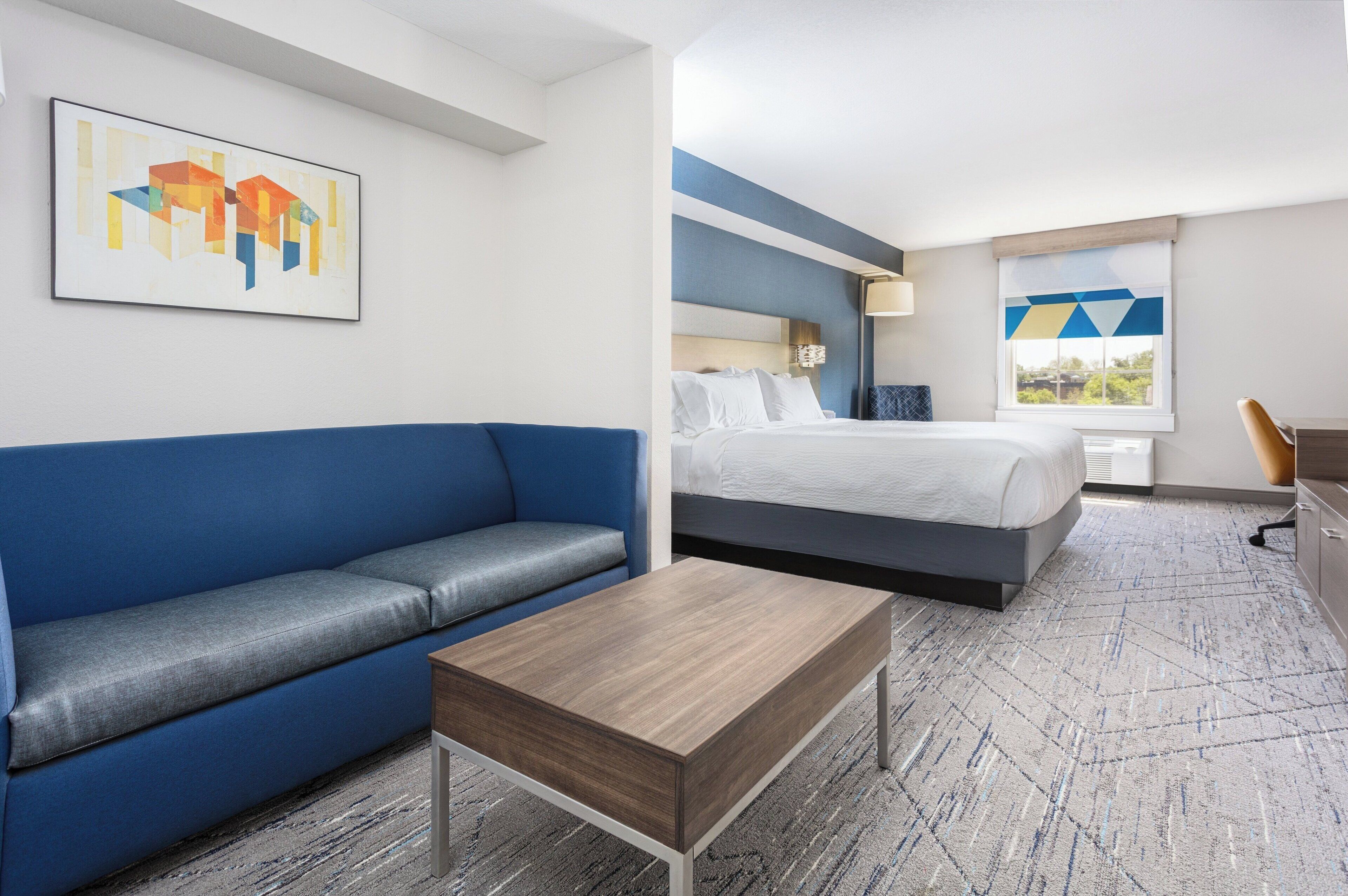 Une chambre d’hôtel avec un canapé bleu, un lit avec une literie blanche, une table basse en bois et un tableau accroché au mur.