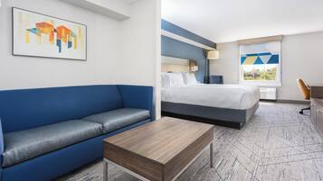 Habitación de hotel con sofá azul, cama con ropa blanca, mesa de centro de madera y un cuadro en la pared.