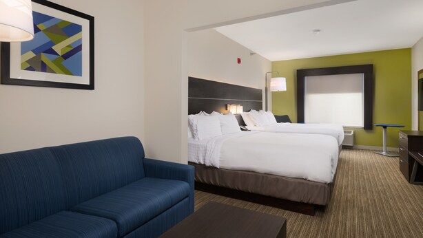 A hotel room with a large bed, a blue sofa, a small table, and a framed abstract painting on the wall. - Holiday Inn Express Hotel & Suites Independence-Kansas City by IHG (Independence)