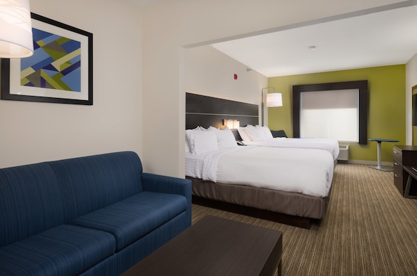 A hotel room with a large bed, a blue sofa, a small table, and a framed abstract painting on the wall.