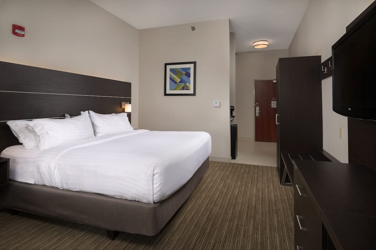 A hotel room with a large bed, a flat-screen TV, a dark wooden dresser, and a framed abstract artwork on the wall.