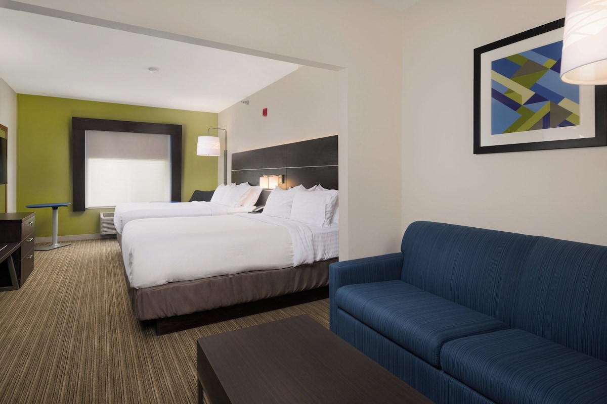 A hotel room with a bed, a blue sofa, a desk, and a lamp.