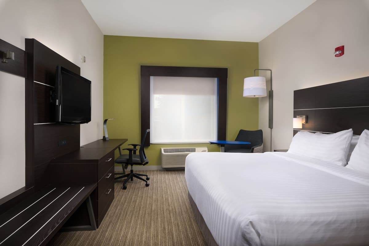 A hotel room with a bed, desk, chair, television, and a window with blinds.