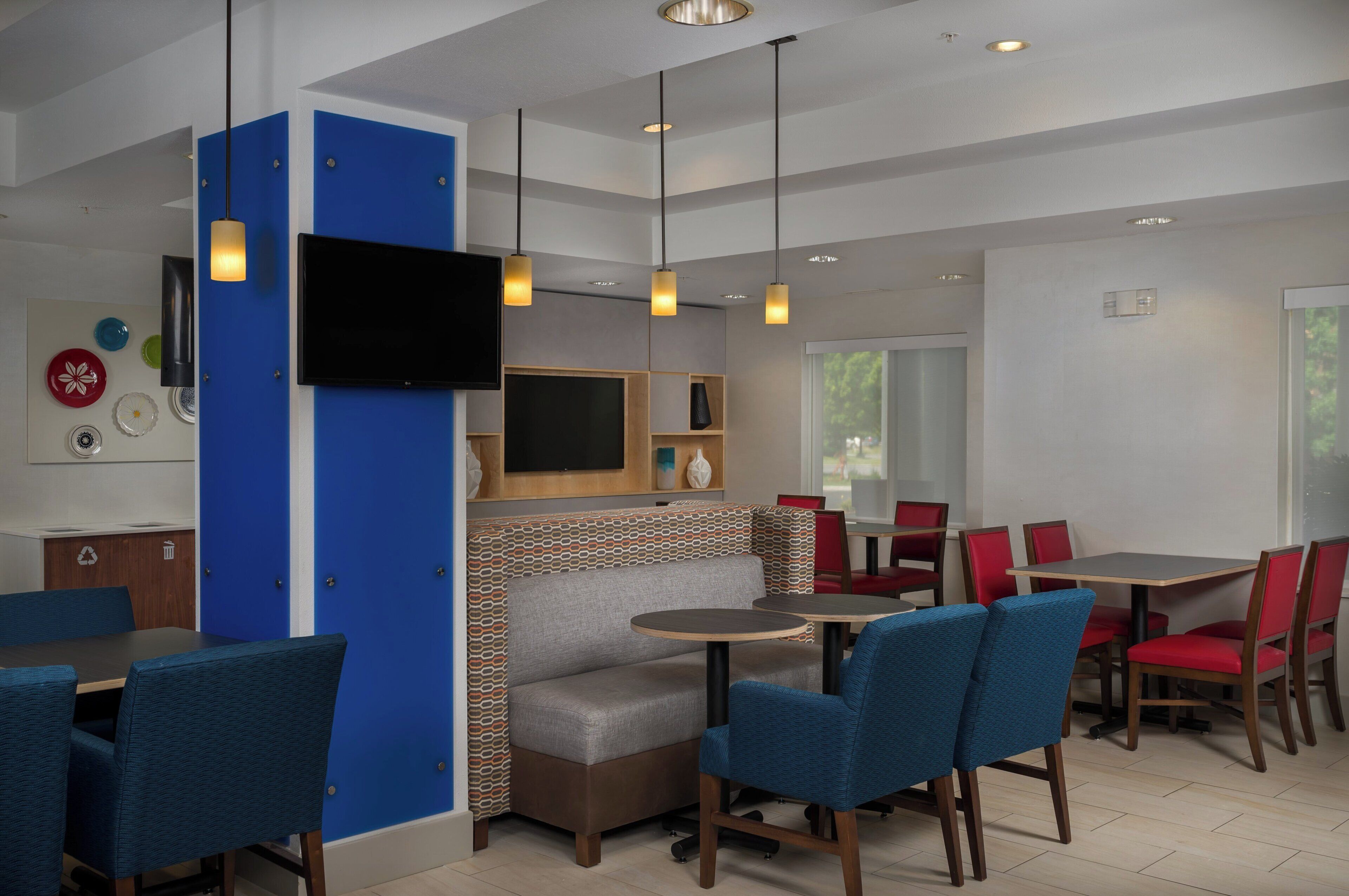 A modern dining area with blue upholstered chairs, a round table, and a television mounted on a blue panel.