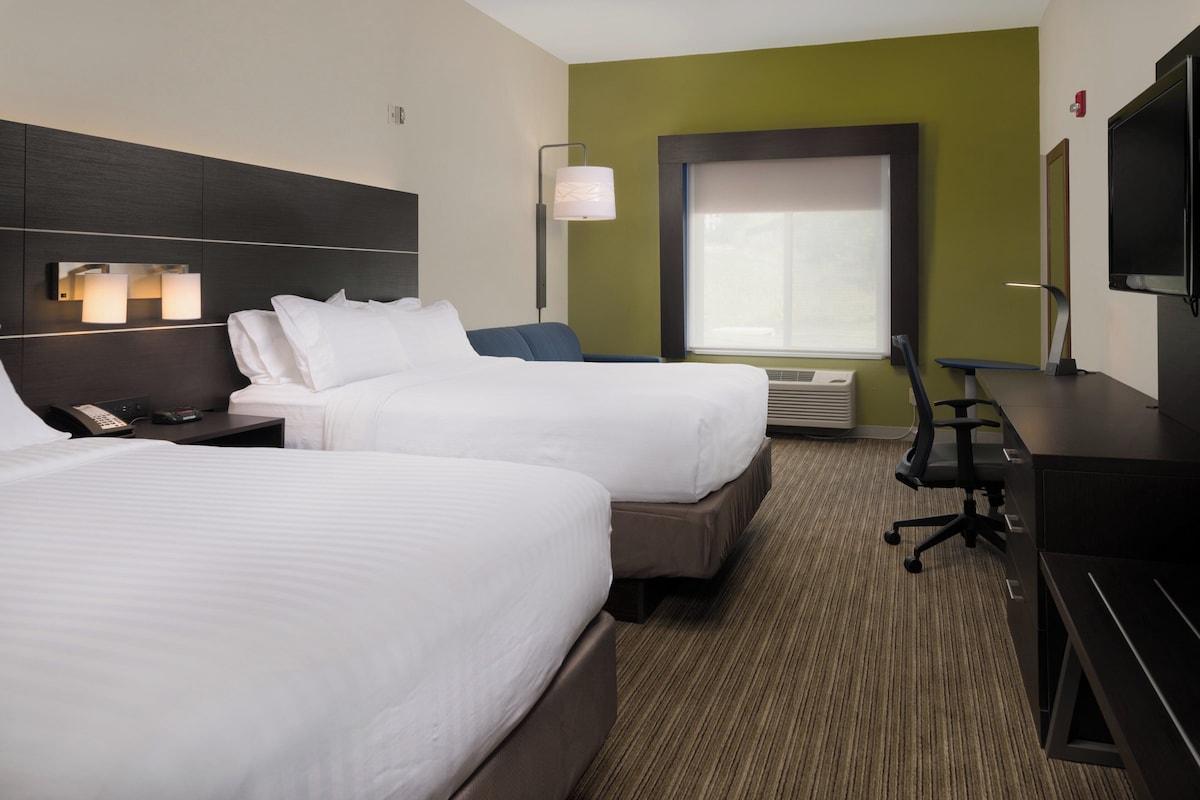 A hotel room with two beds, a desk, a chair, a phone, a lamp, and a window.