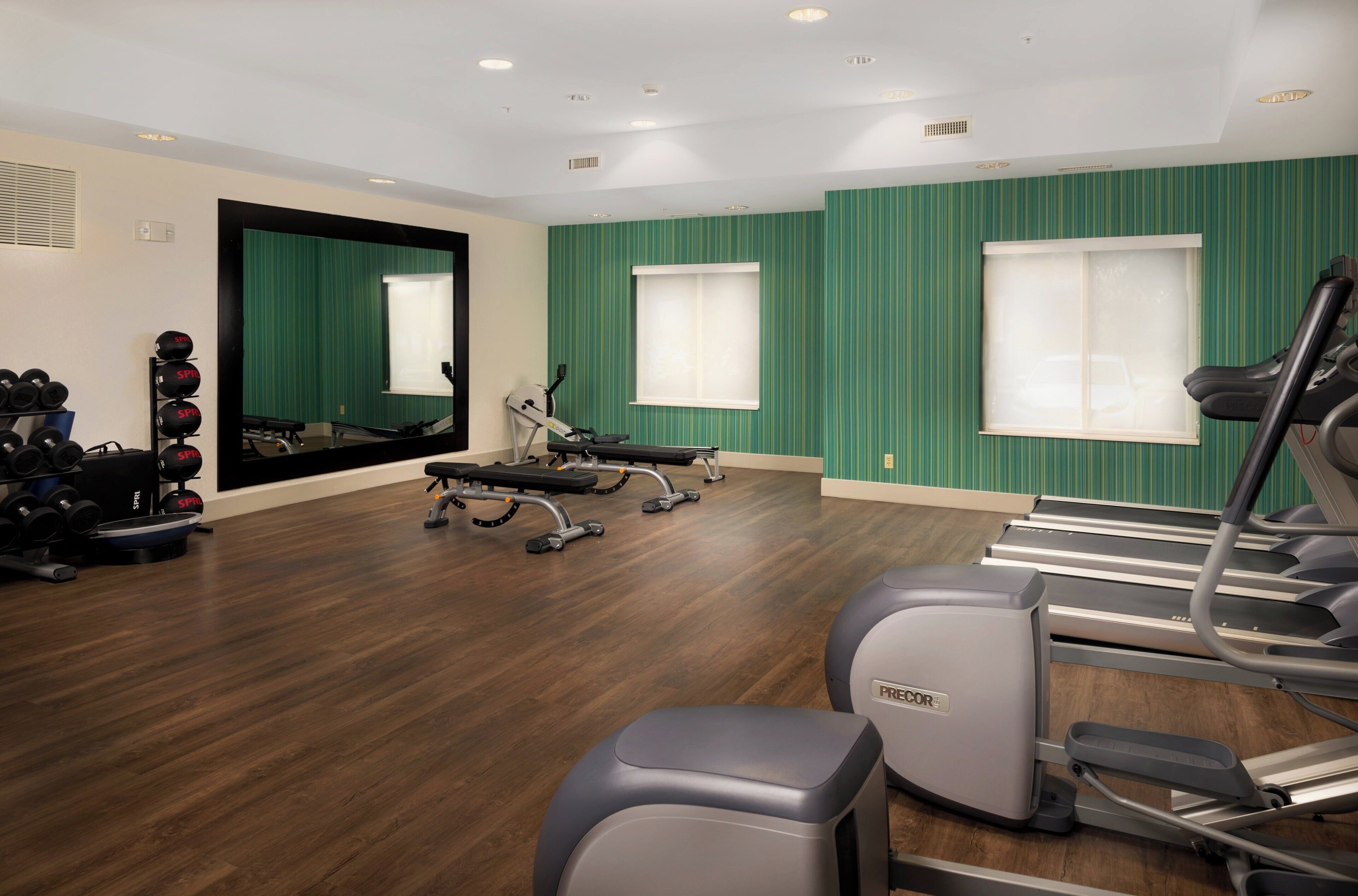 Een sportschool met fitnessapparatuur, een spiegel en muren met groene strepen.