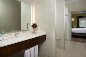A hotel bathroom with a double sink, a mirror, and a glass shower enclosure.