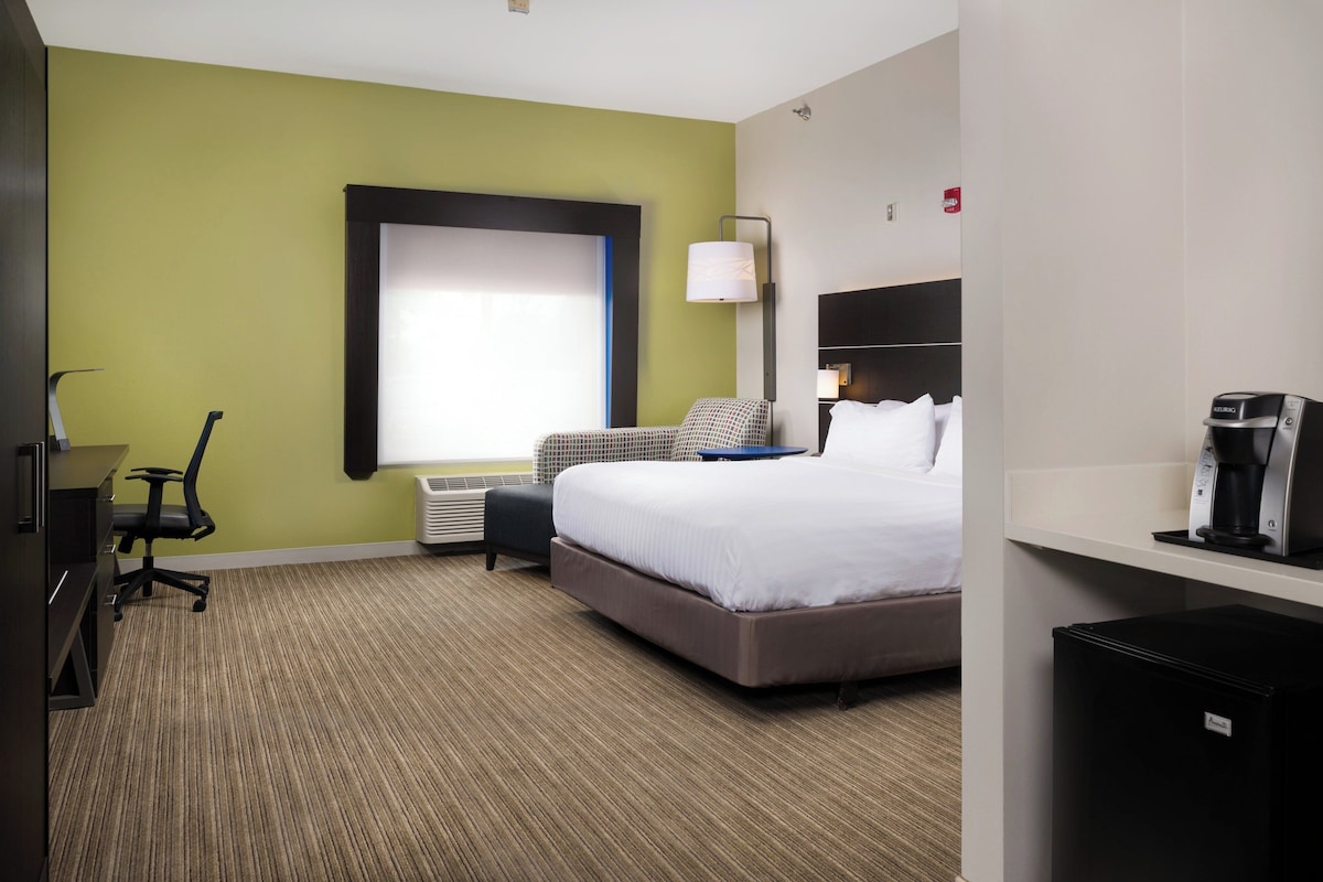 A hotel room with a bed, a desk, a chair, a lamp, and a coffee maker.