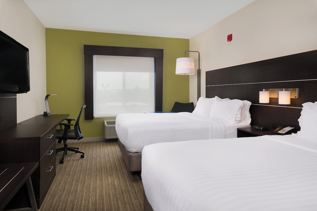 A hotel room with two beds, a desk, a chair, a television, and a window with blinds.