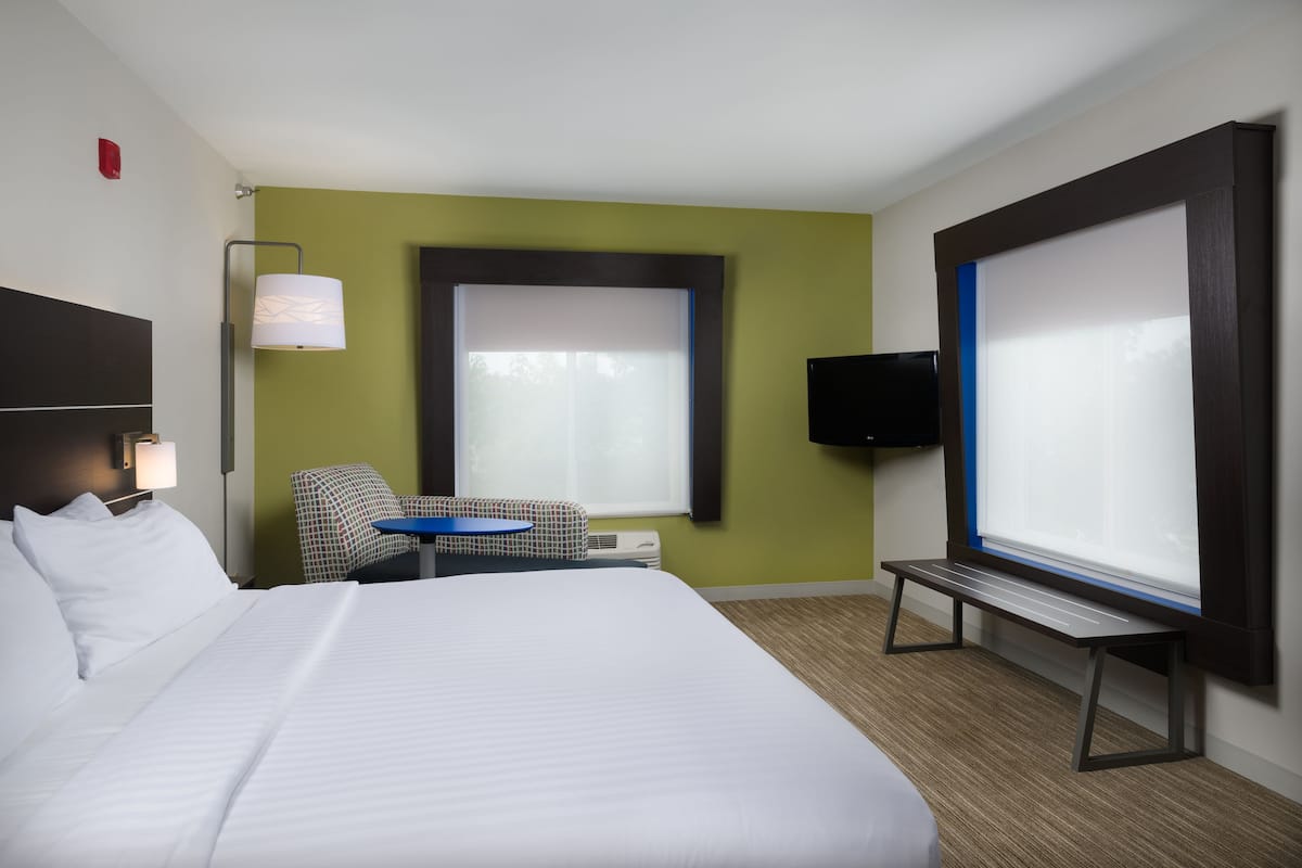 A hotel room with a large bed, a desk with a chair, a TV, and a window with blinds.