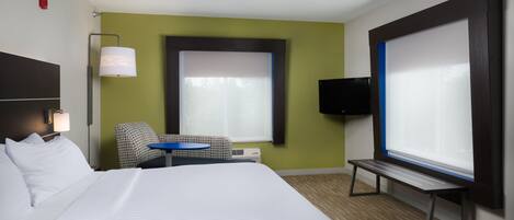 A hotel room with a large bed, a desk with a chair, a TV, and a window with blinds.