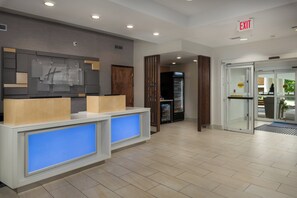A hotel reception area with a modern design, including a reception desk, a glass door entrance, and a visible exit sign.