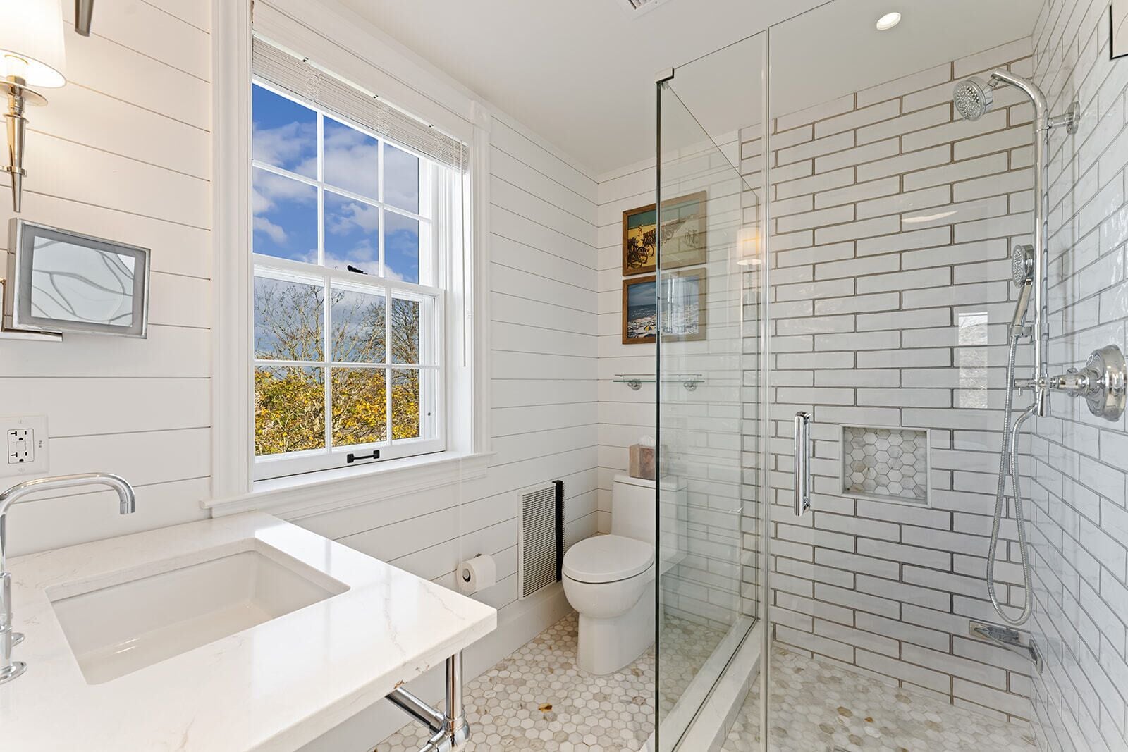 Un baño moderno con un ventanal grande, una ducha con cerramiento de vidrio y un lavamanos blanco.