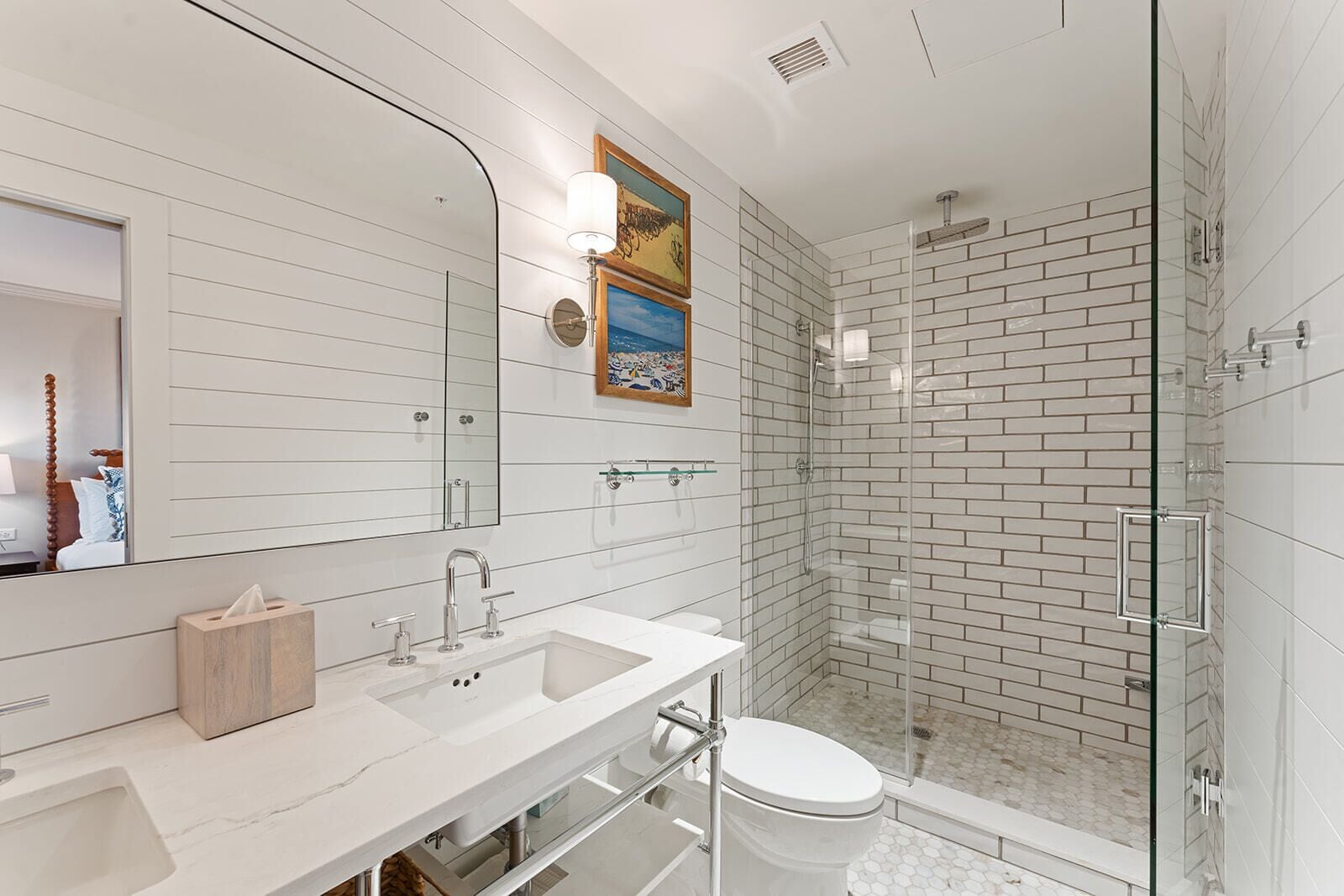 Un baño moderno con un espejo grande, azulejos blancos tipo metro, cabina de ducha de vidrio y tocador de madera.
