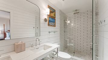 Un baño moderno con un espejo grande, azulejos blancos tipo metro, cabina de ducha de vidrio y tocador de madera.
