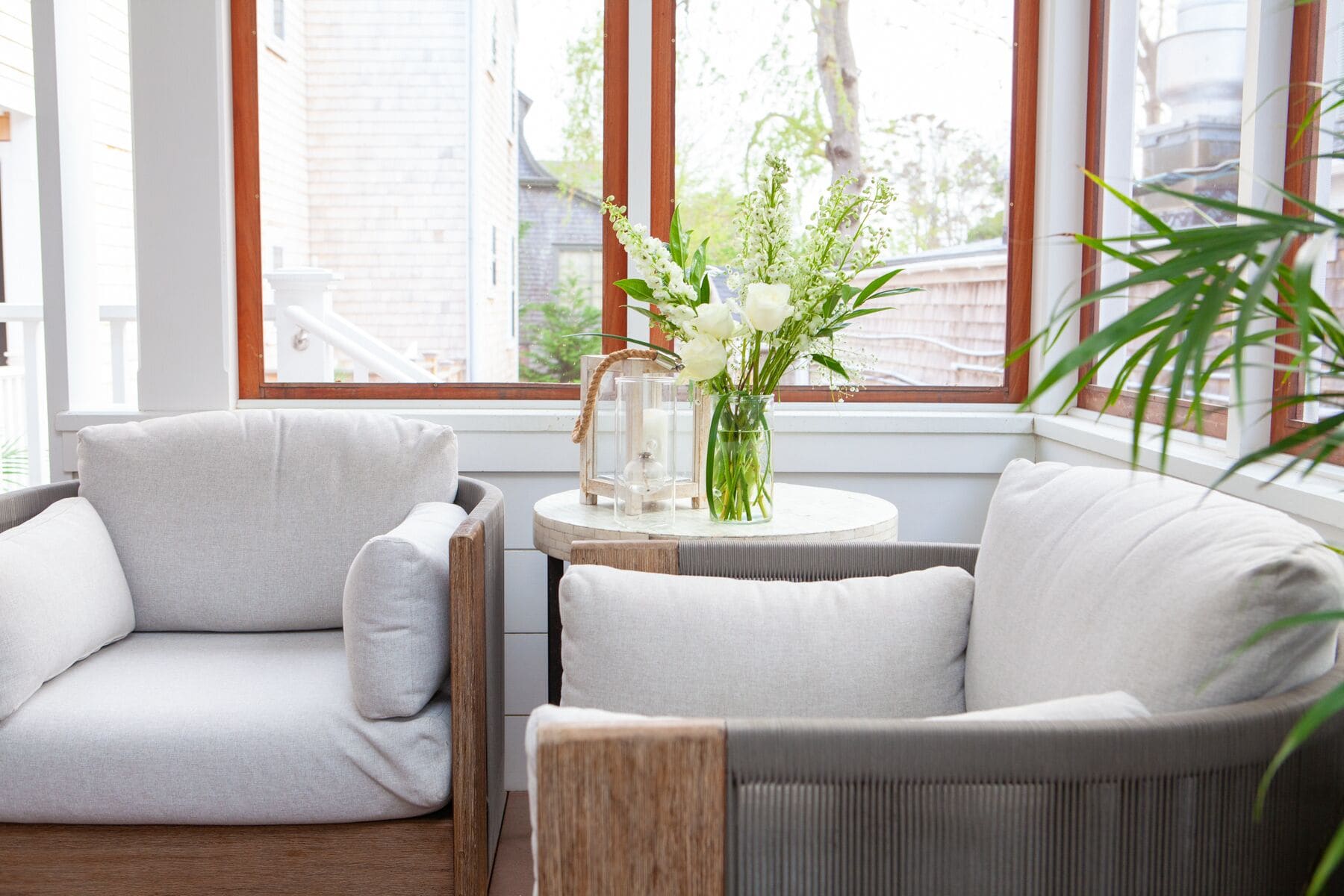 Un coin salon accueillant avec deux fauteuils gris à revêtement rembourré, une petite table ronde ornée d’un vase de fleurs et une fenêtre donnant sur des immeubles.