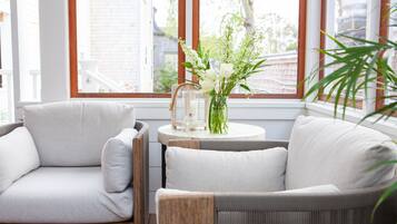 Un rincón acogedor con dos sillones grises tapizados, una pequeña mesa redonda con un florero y una ventana con vistas a edificios.