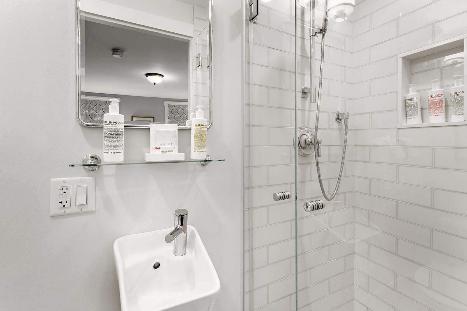 Une salle de bain moderne avec une douche à parois de verre, un lavabo blanc et une étagère contenant des articles de toilette.