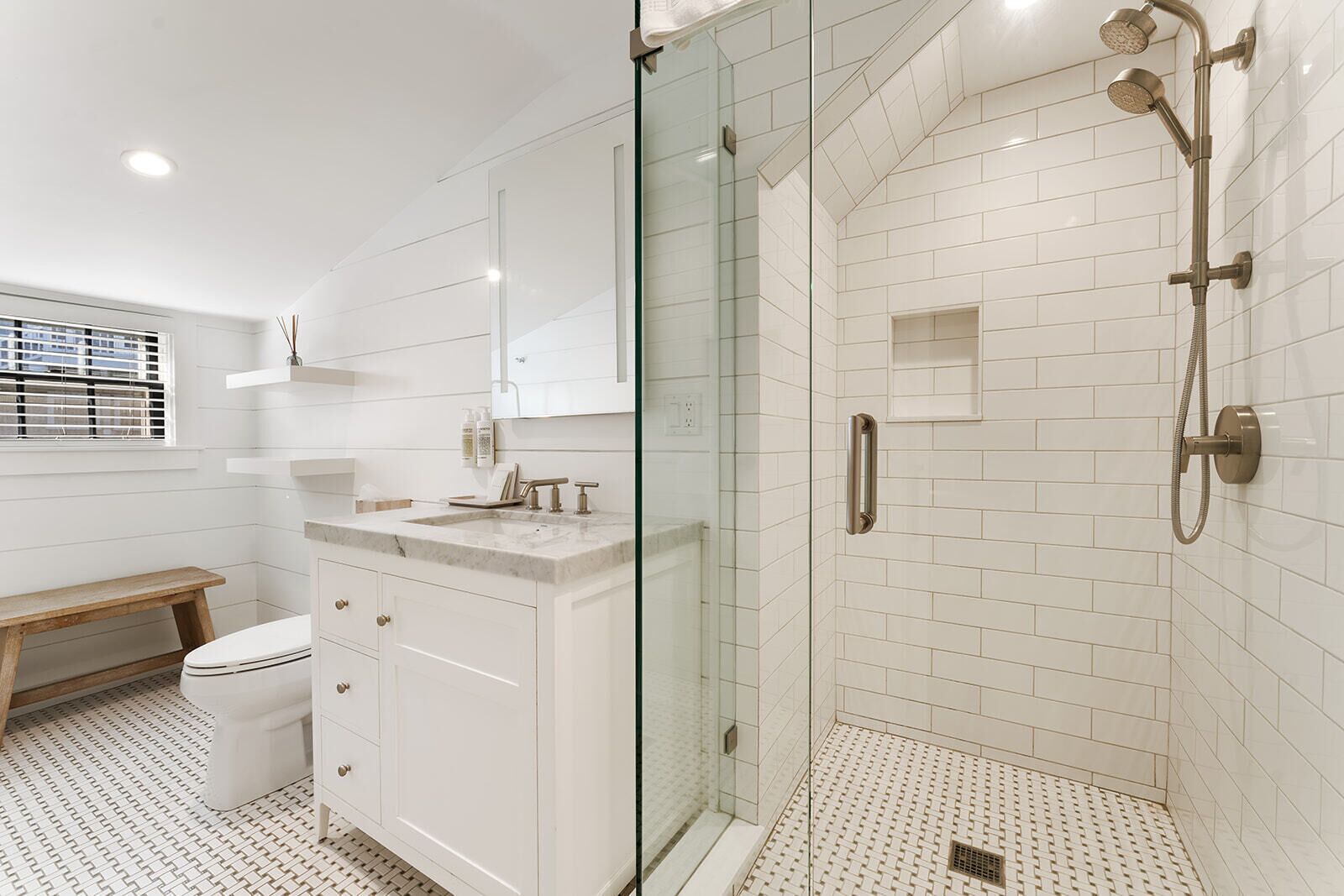 Un baño moderno con ducha de vidrio, paredes de azulejos blancos y encimera de mármol.