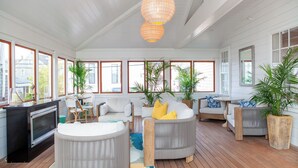 A spacious living room with a wooden floor, white walls, and large windows. There are several seating areas, including a grey sofa and a round table. - Nantucket Resort Collection (Nantucket)