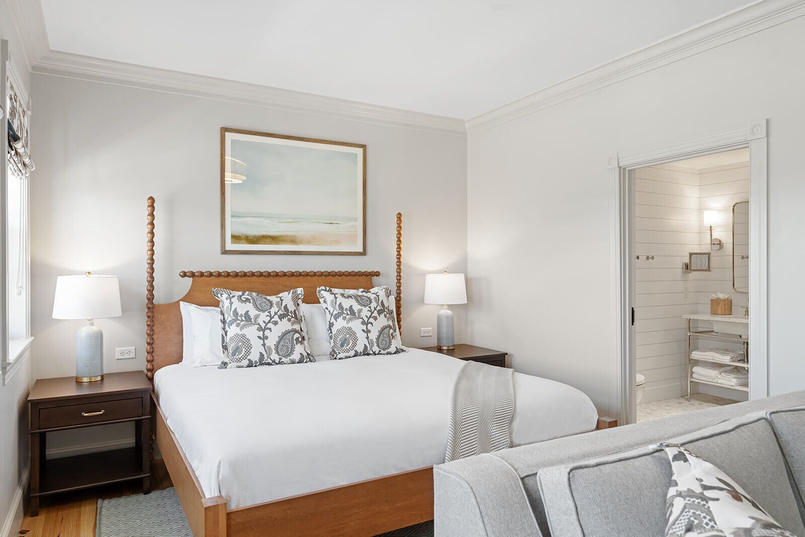A neatly arranged hotel room with a large bed, two bedside tables with lamps, a framed artwork above the bed, and a view into the bathroom through an open door.