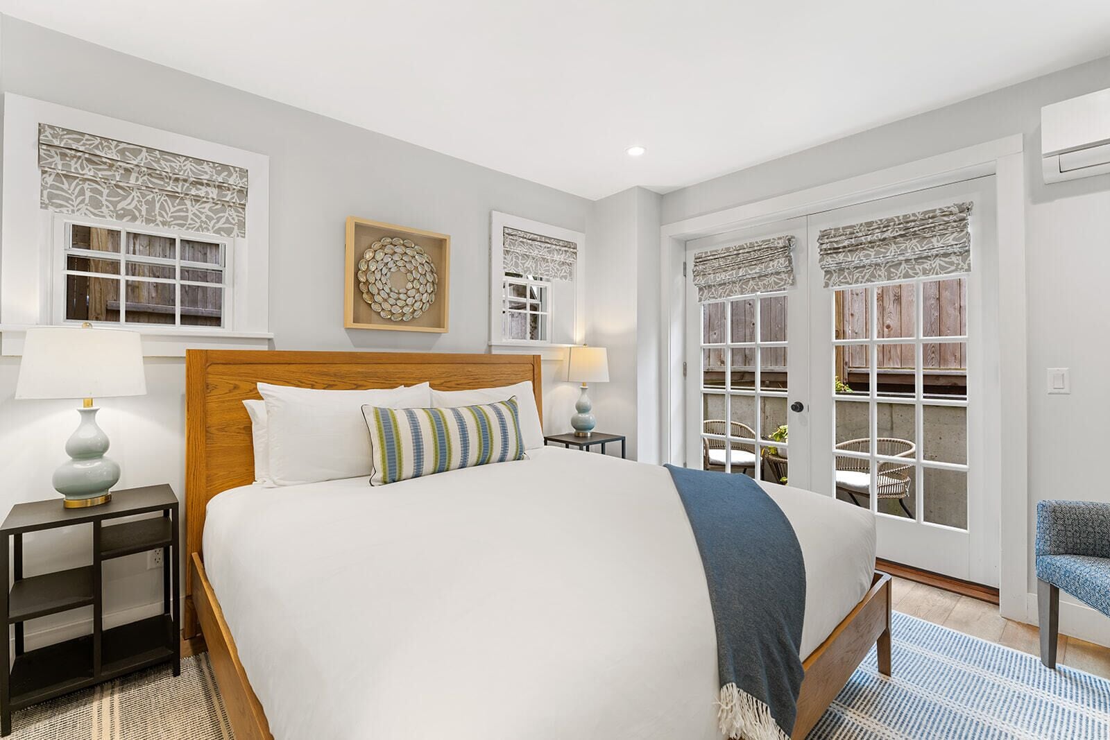 A neatly arranged bedroom with a large bed, bedside tables, a chair, and a view through a window with patterned curtains.