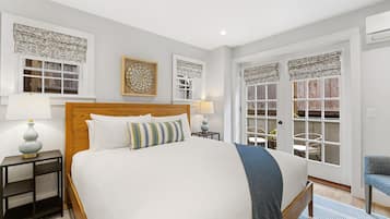 A neatly arranged bedroom with a large bed, bedside tables, a chair, and a view through a window with patterned curtains.