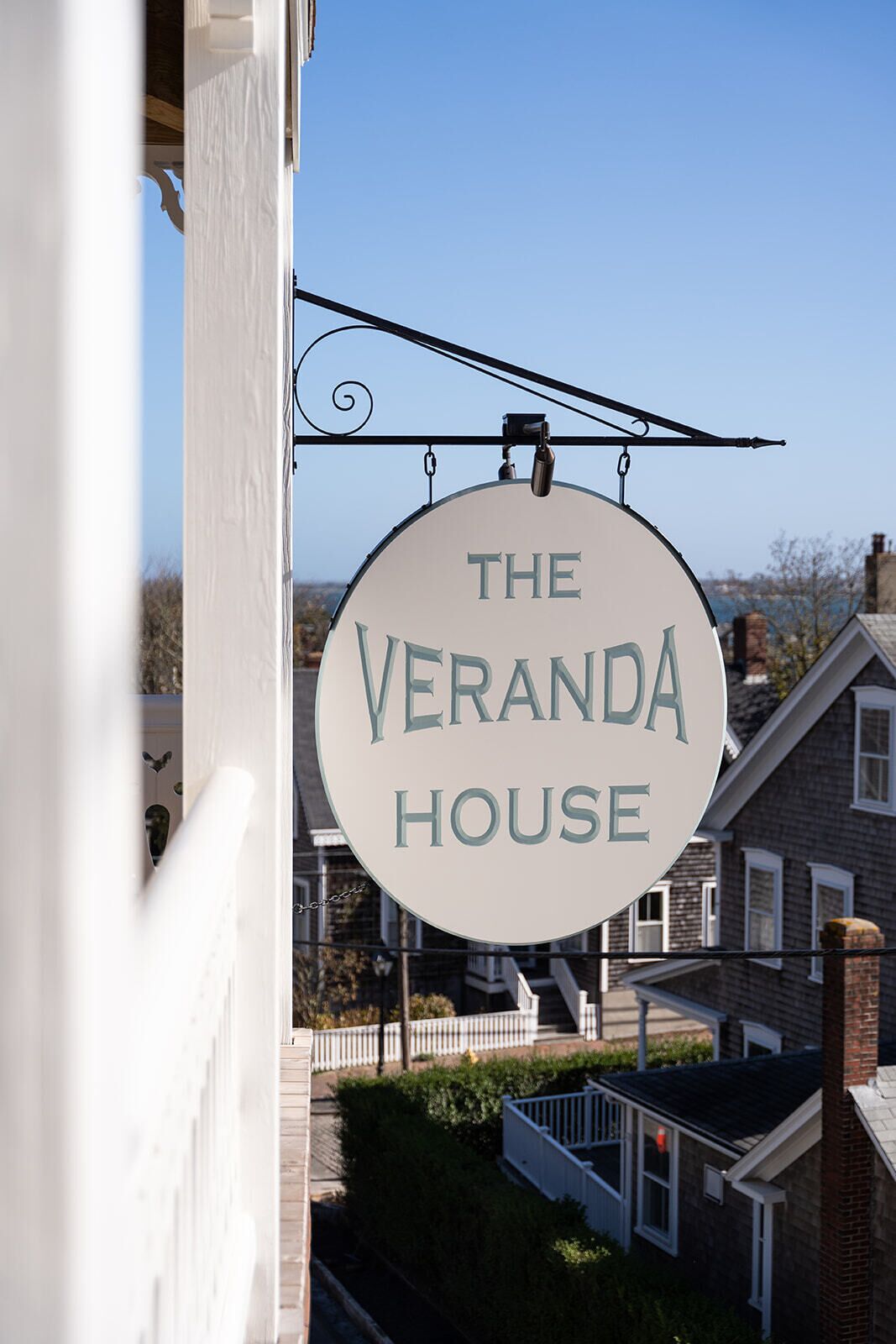 Un panneau circulaire portant l’inscription « THE VERANDA HOUSE » est suspendu à un bâtiment.
