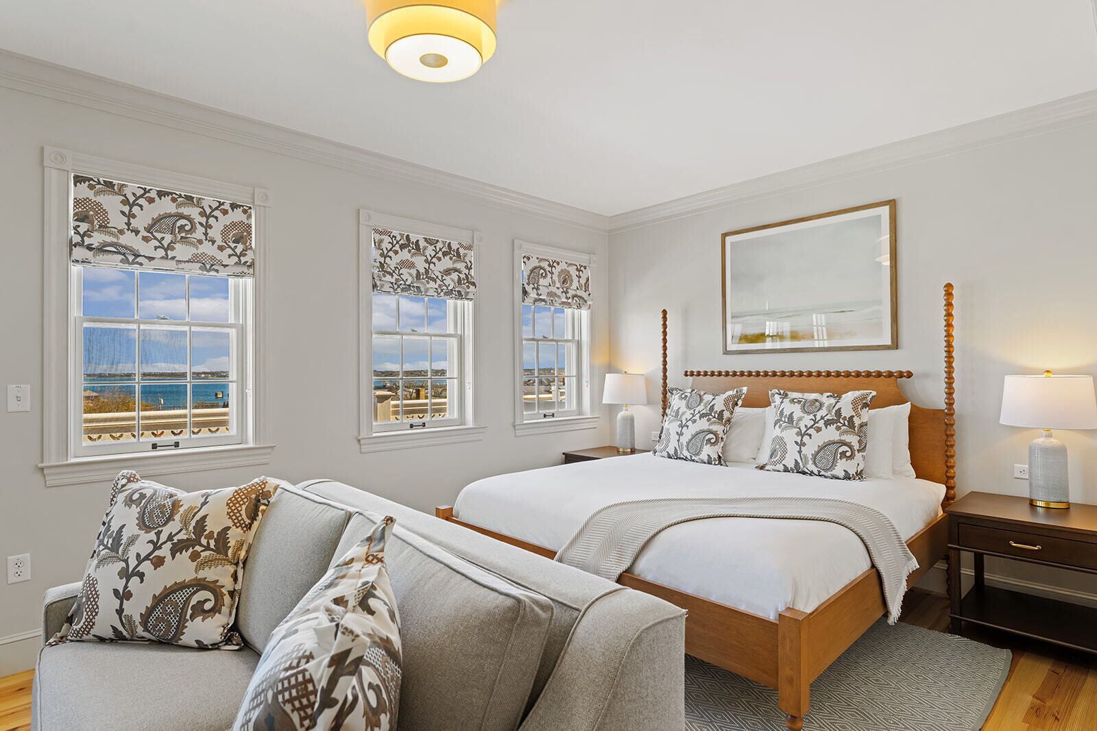 Una habitación de hotel con una cama grande, un sofá y tres ventanas con cortinas estampadas.