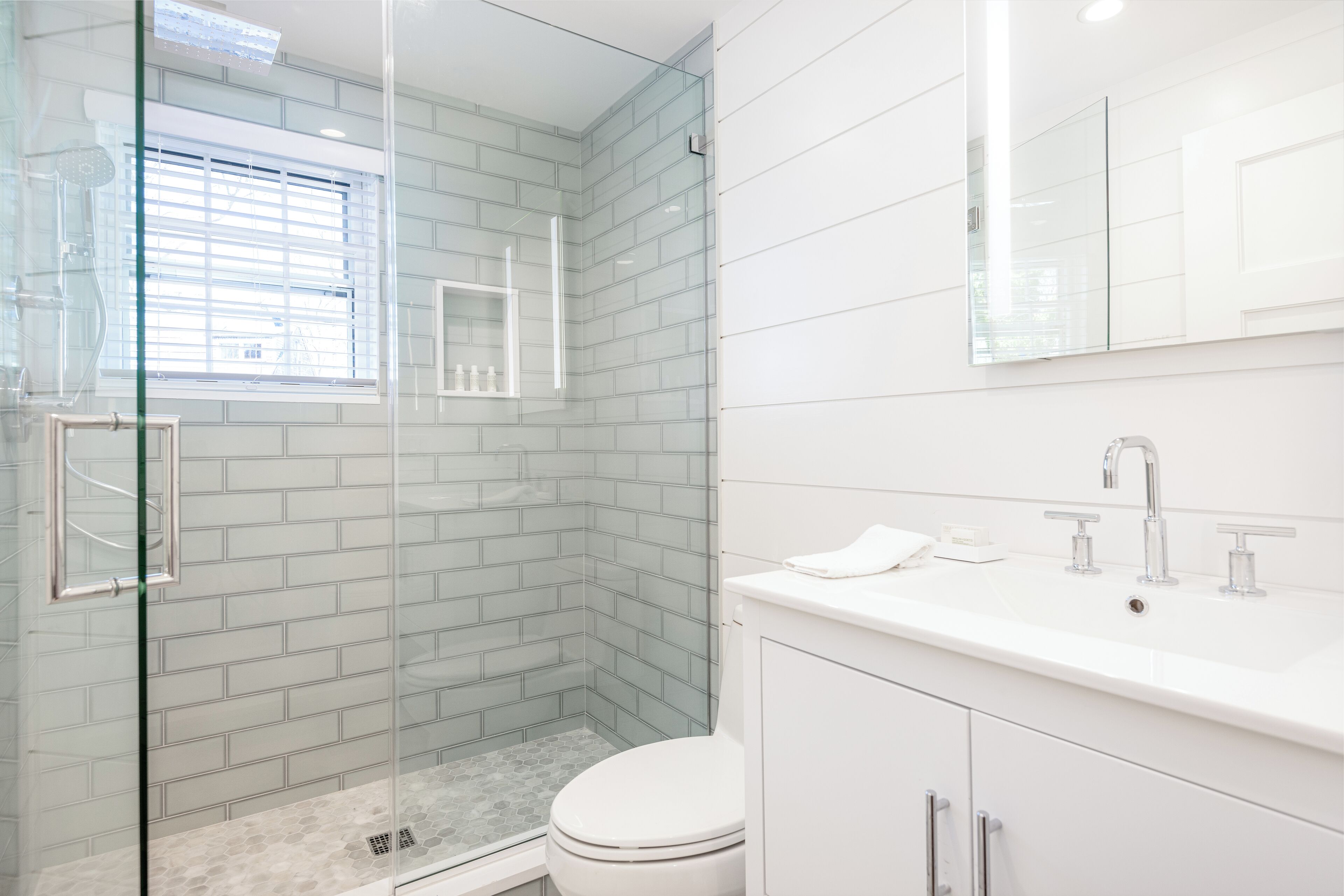 A modern bathroom with a glass-enclosed shower, a toilet, and a sink with a mirror above it.