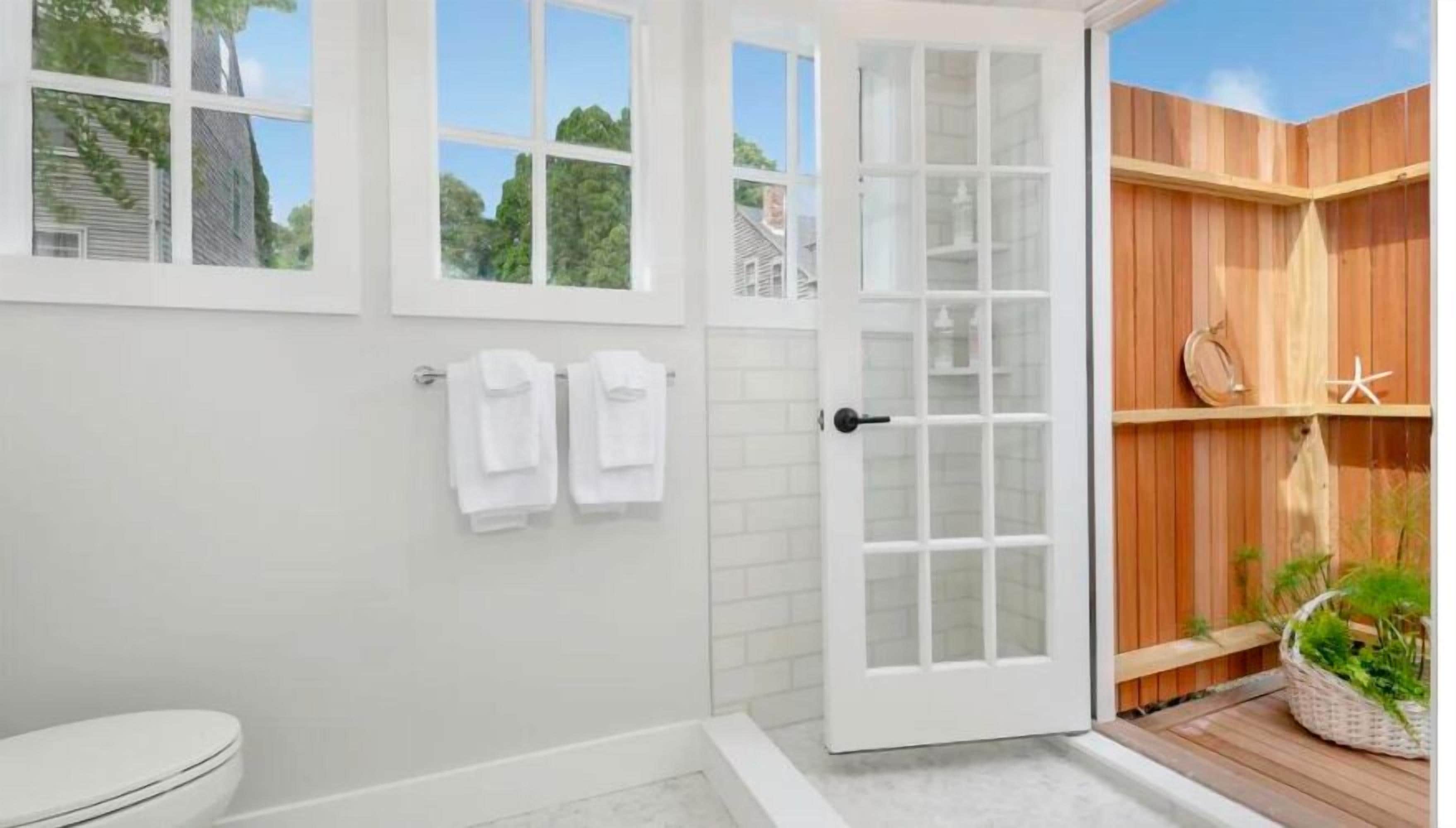 A modern bathroom with a toilet, a shower area, and a wooden deck with plants.