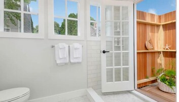 A modern bathroom with a toilet, a shower area, and a wooden deck with plants.