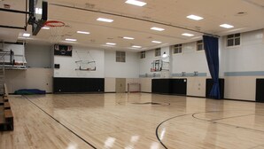 Un gimnasio con cancha de baloncesto, marcador de puntos y aro.