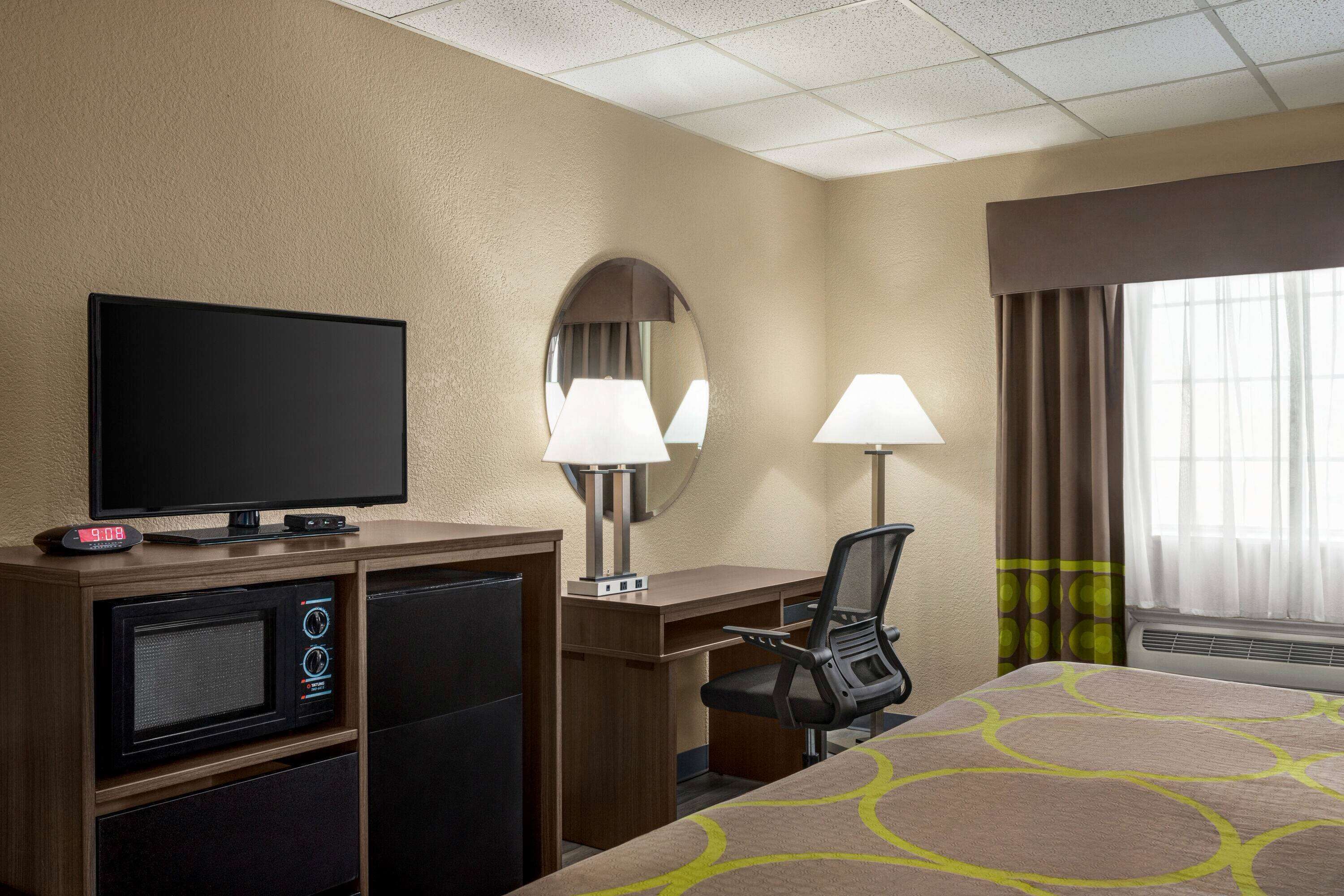 A hotel room with a bed, a desk, a television, a microwave, and a mirror.