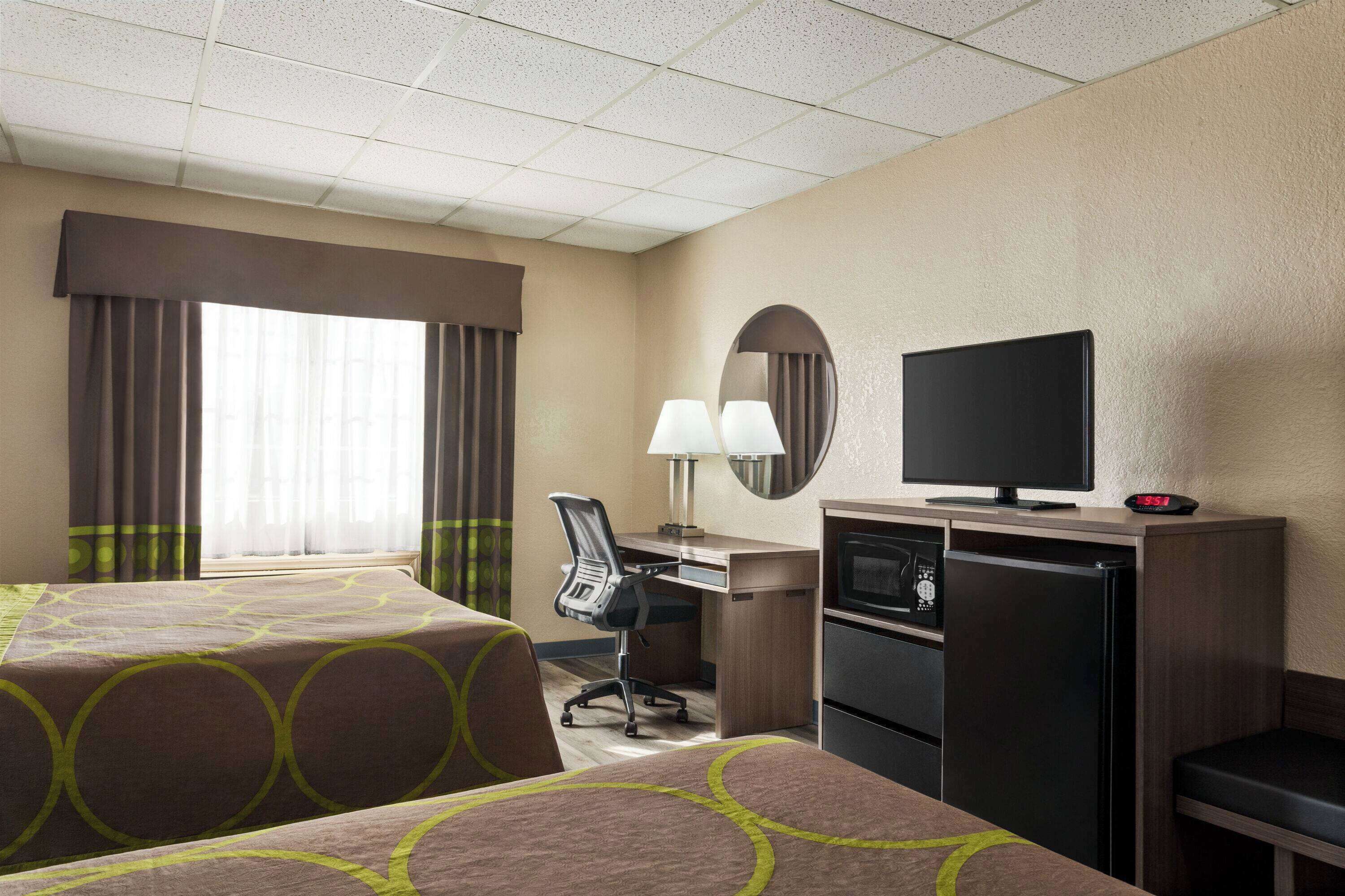 A hotel room with two beds, a desk with a computer, a television, and a refrigerator.